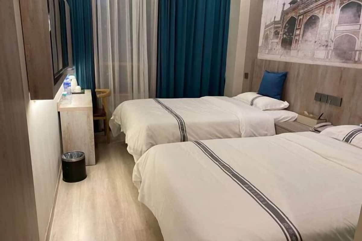 A hotel room with two beds, a desk with toiletries, a trash bin, and a wall with a decorative mural.