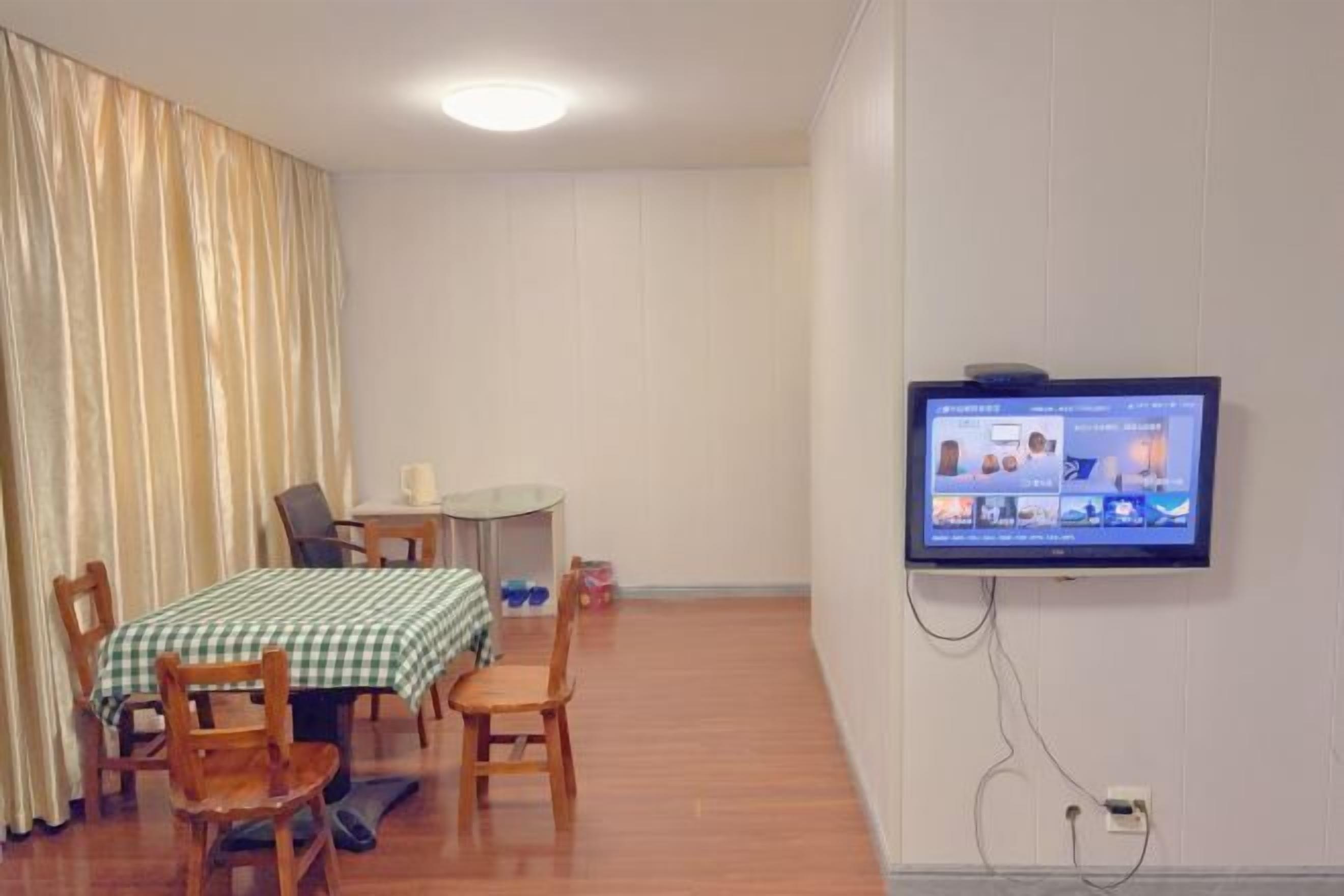 Ein Zimmer mit Esstisch, Stühlen, einem an der Wand befestigten Fernseher und einem Vorhang.