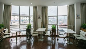 A modern dining area with multiple tables and chairs, large windows offering a city view, and potted plants. - Shaoxing Mingdu Business Hotel (Shaoxing)