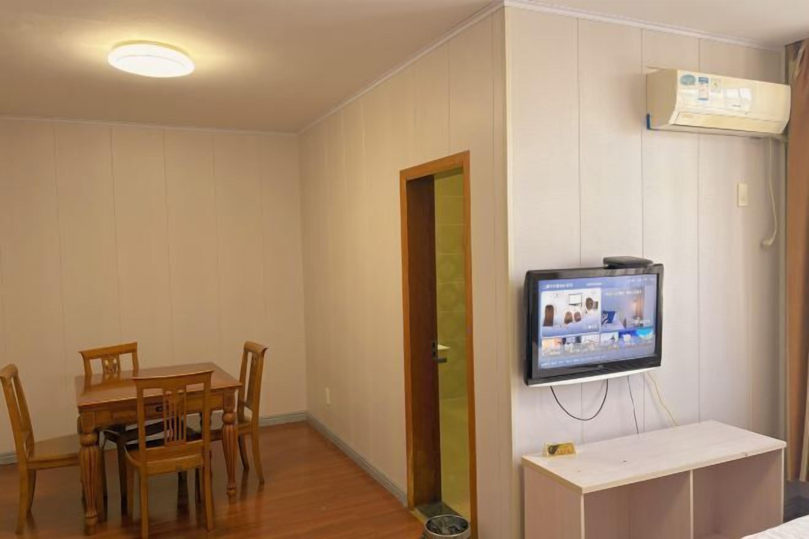 A room with a dining table and chairs, a television, and an air conditioning unit.