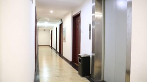 Ein Hotelgang mit gefliestem Boden, Türen und einem Aufzug.