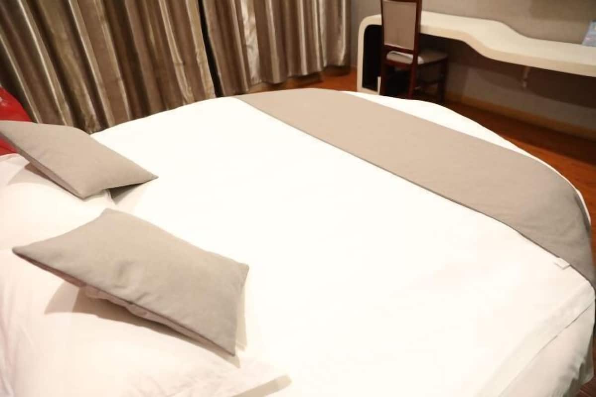 Una cama bien hecha con almohadas y una manta, una silla y una encimera en una habitación con cortinas.