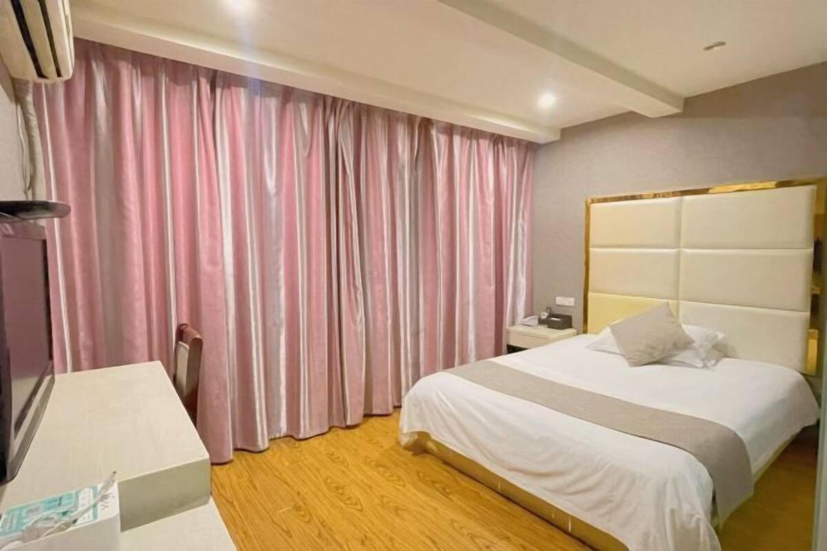 Habitación de hotel con cama, mesita de noche, lámpara y ventana con cortinas.