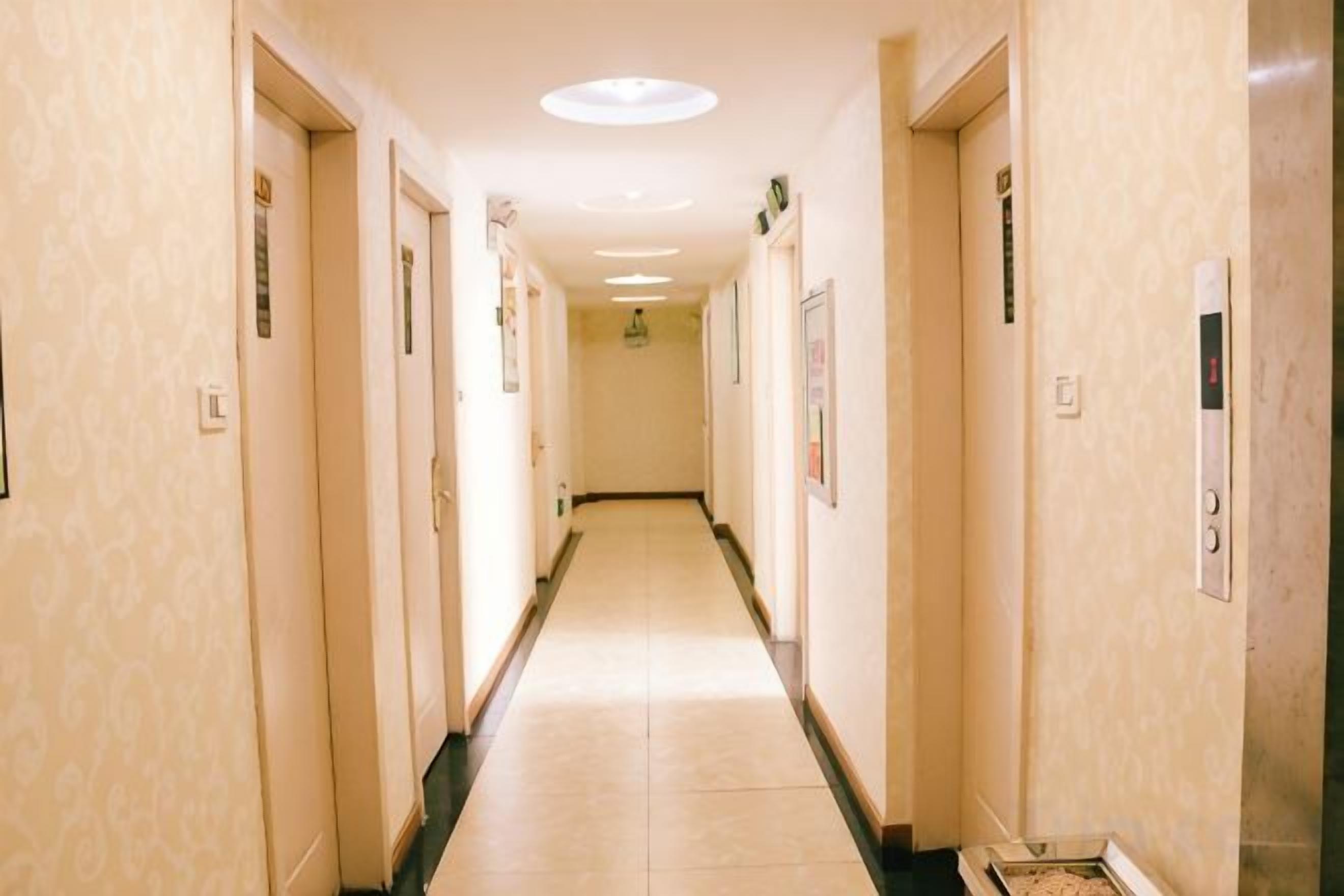 Un corridoio d'albergo con porte su entrambi i lati, pavimento piastrellato e lampadario al soffitto.