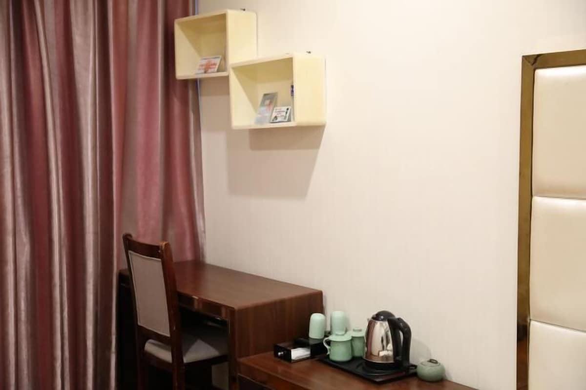 A small room with a wooden desk, a chair, a shelf with books, and a coffee maker.