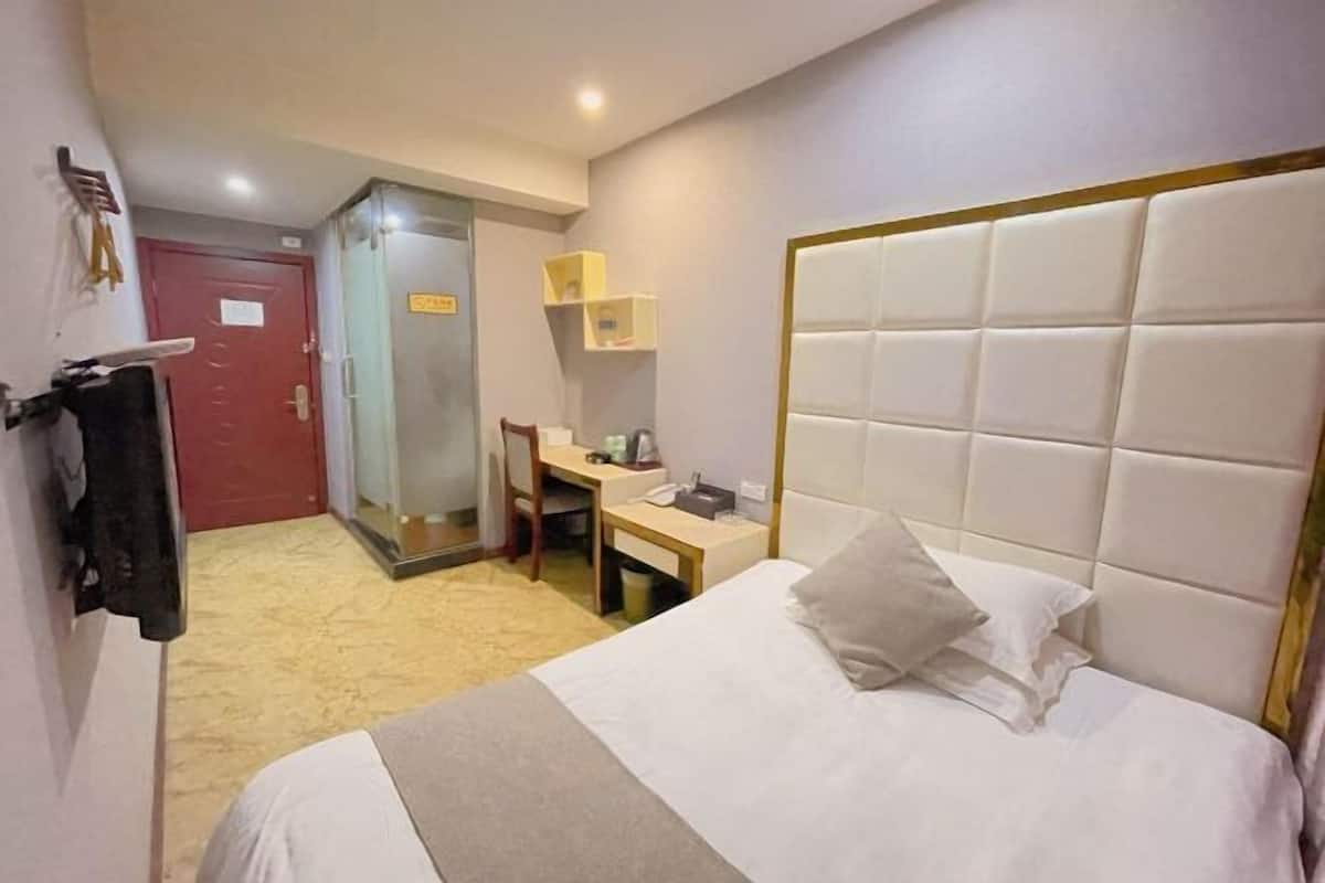 Habitación de hotel con cama, escritorio, silla y zona de ducha.