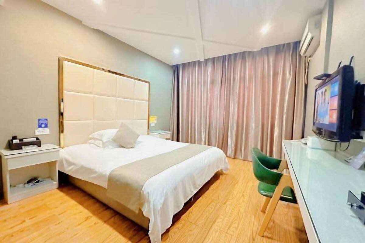 Una habitación de hotel con cama, escritorio, silla, televisor y cortinas.