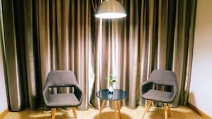Ein Zimmer mit zwei grauen Sesseln, einem kleinen runden Tisch mit einer Vase und einer Lampe.