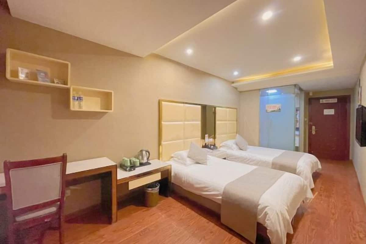 Una habitación de hotel con dos camas, un escritorio, una silla y un pequeño estante con artículos de aseo.