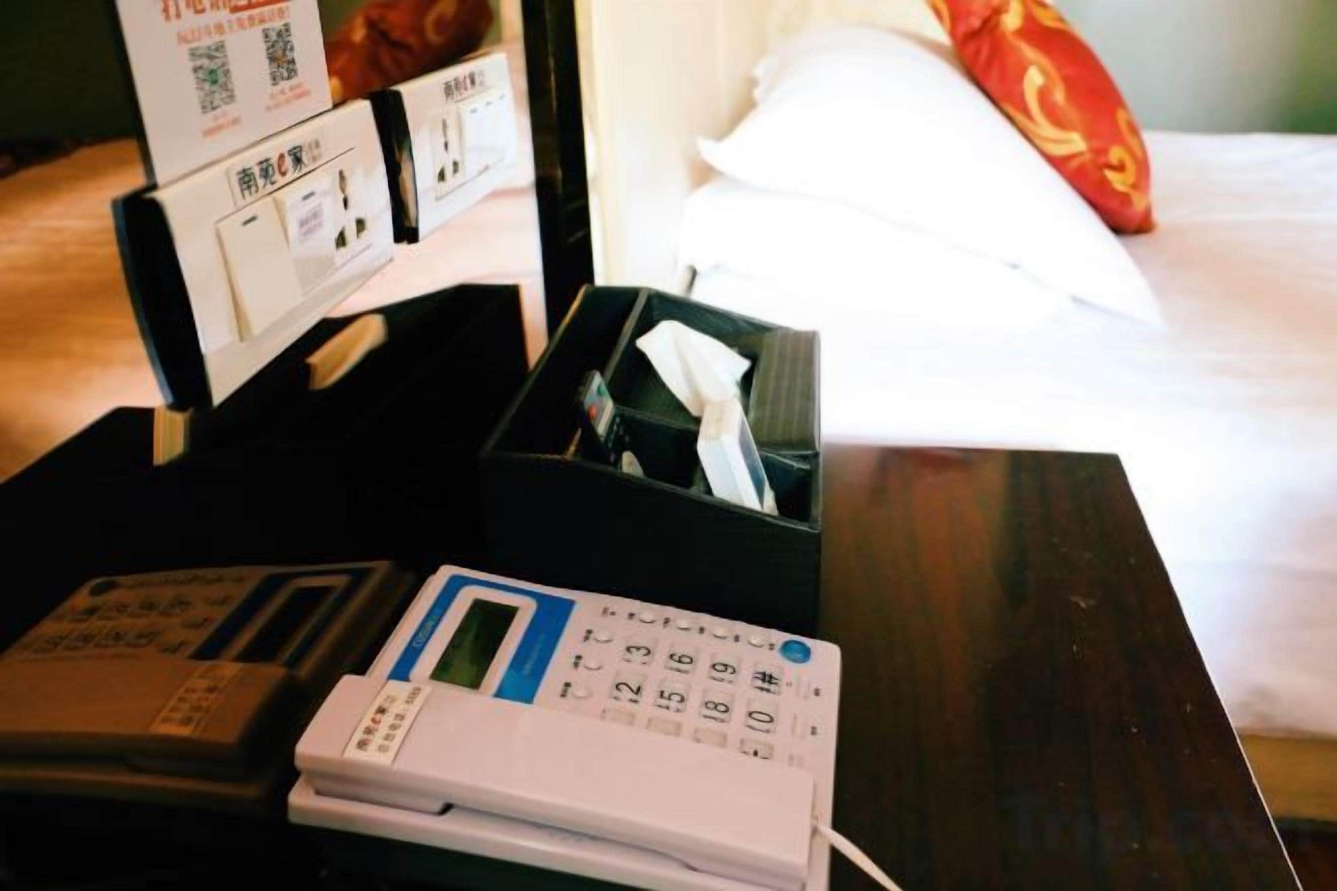 Habitació d'hotel amb un llit, una taula de nit amb un telèfon, una caixa de mocadors i un panell de control fixat a la paret.