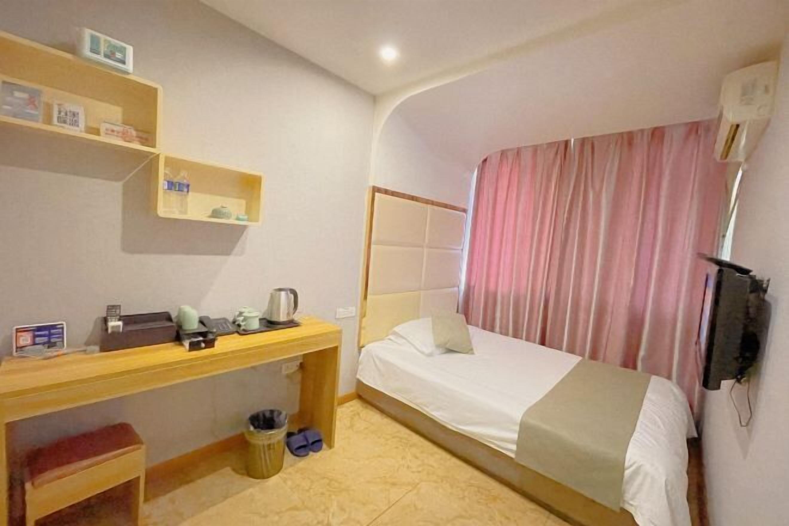 A hotel room with a bed, a desk, a chair, a trash bin, and a TV mounted on the wall.