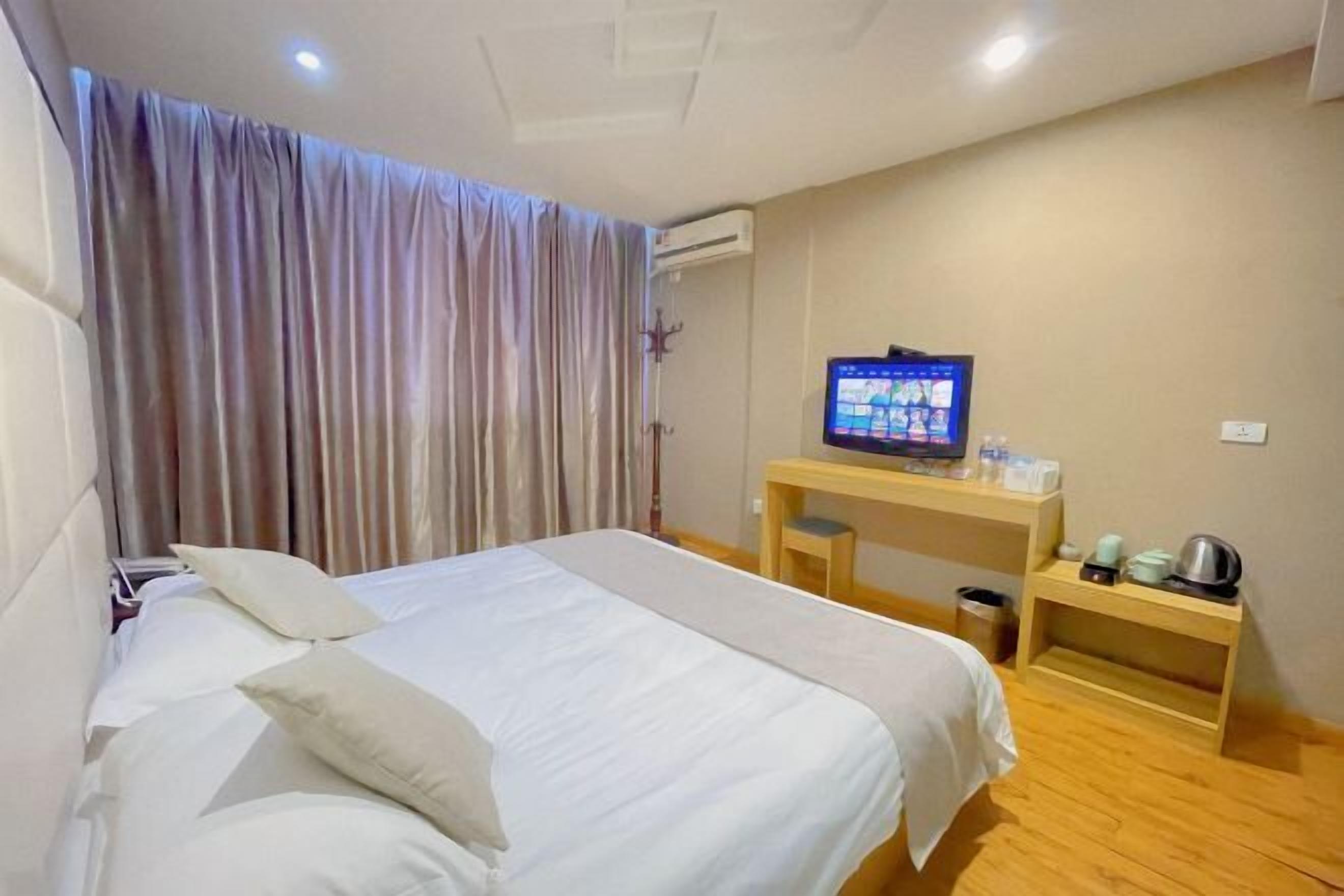 A hotel room with a bed, a desk, a television, and a window with curtains.