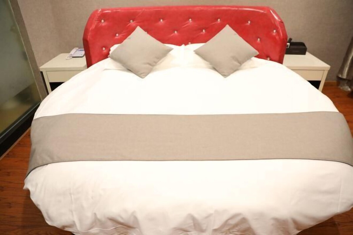 A bed with a red headboard, white bedding, and two pillows.