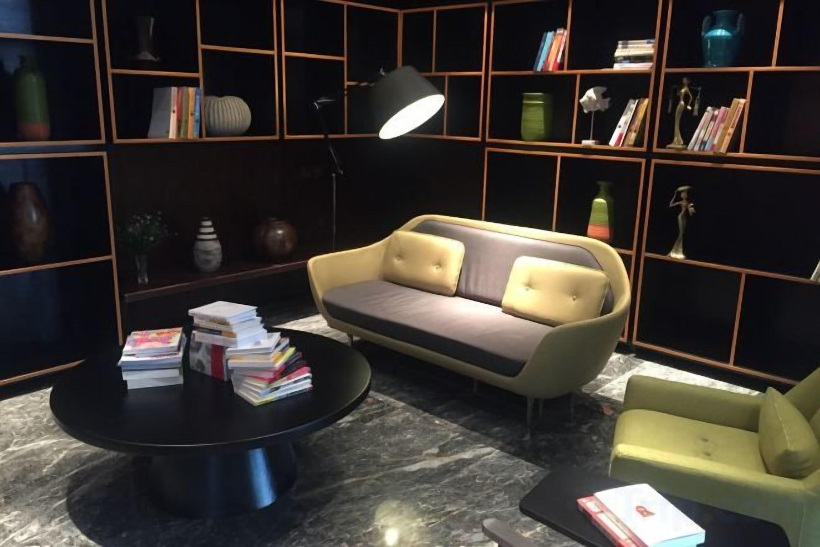 A modern living room with a sofa, armchair, and coffee table, surrounded by bookshelves and decorative items.