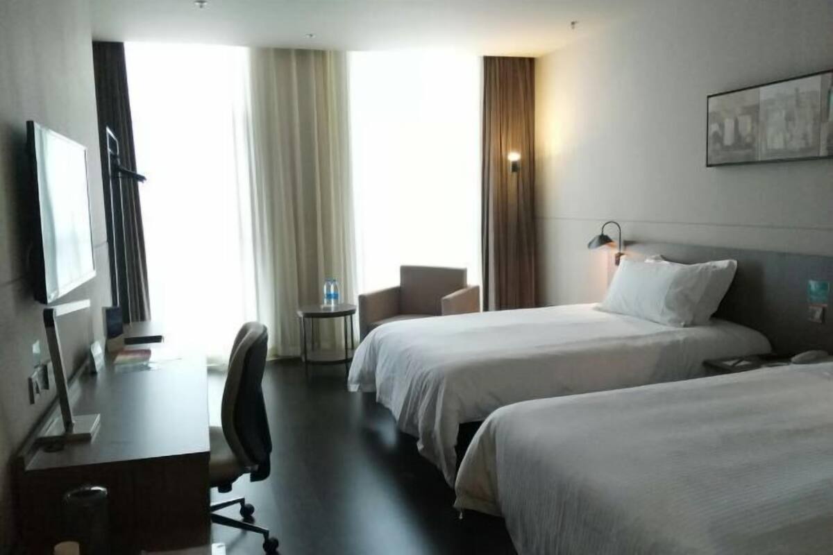 Une chambre d’hôtel avec deux lits, un bureau, une chaise, une télévision et une fenêtre avec des rideaux.