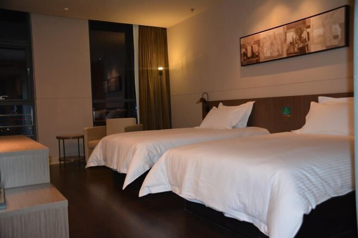 A hotel room with two beds, a small seating area, and a large window.