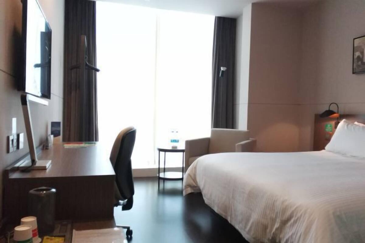 Une chambre d’hôtel avec un lit, un bureau, une chaise, une télévision et une fenêtre avec des rideaux.