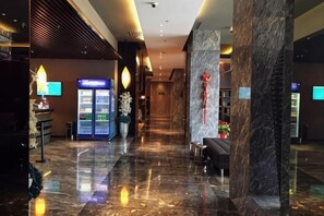 A hotel lobby with a marble floor, a reception desk, a refrigerator, and a decorative wall with a red emblem. - Jinjiang Inn Select (Dongying Kenli Petrochemical Building) (Dongying)