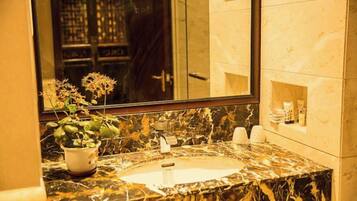 Un baño con lavamanos de mármol, una planta en maceta y un espejo que refleja una puerta y un muro con azulejos.