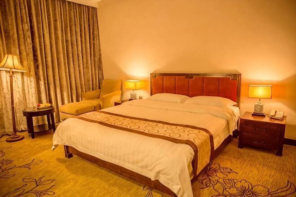 A hotel room with a bed, two bedside tables, a chair, a lamp, and a curtain.