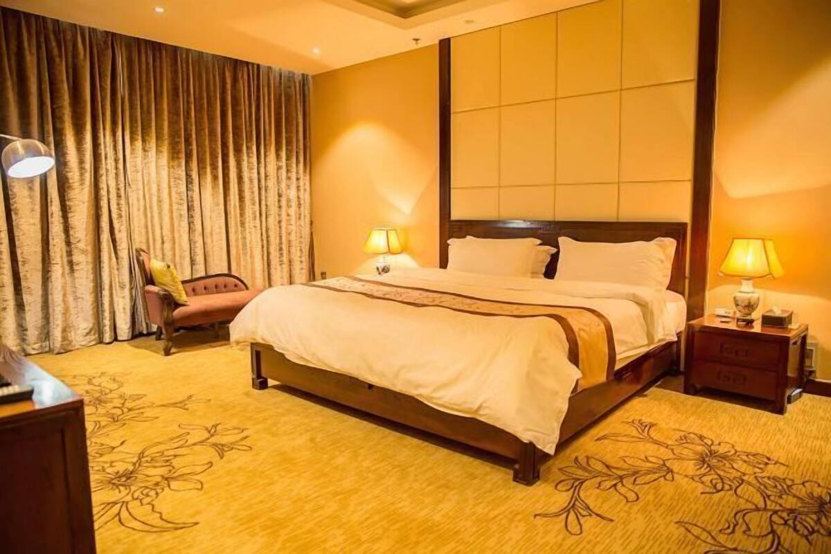 A hotel room with a large bed, two bedside lamps, a wooden nightstand, a chair, and a curtain.