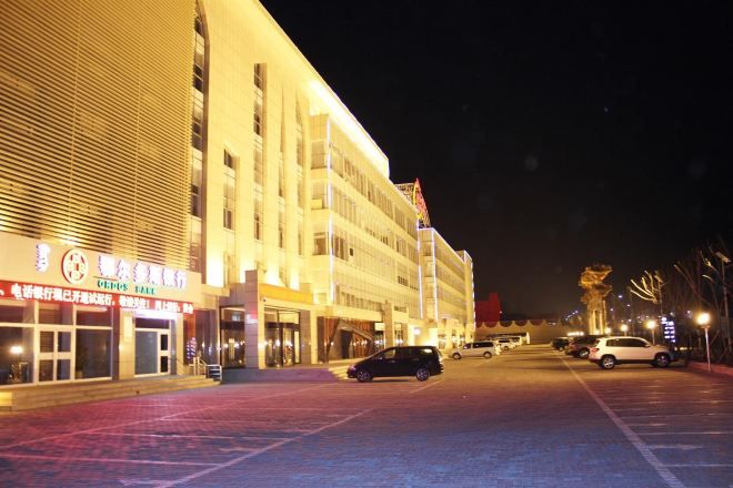 Monikerroksinen rakennus, jossa on parkkipaikka, ja muutamia autoja on pysäköity sen eteen.