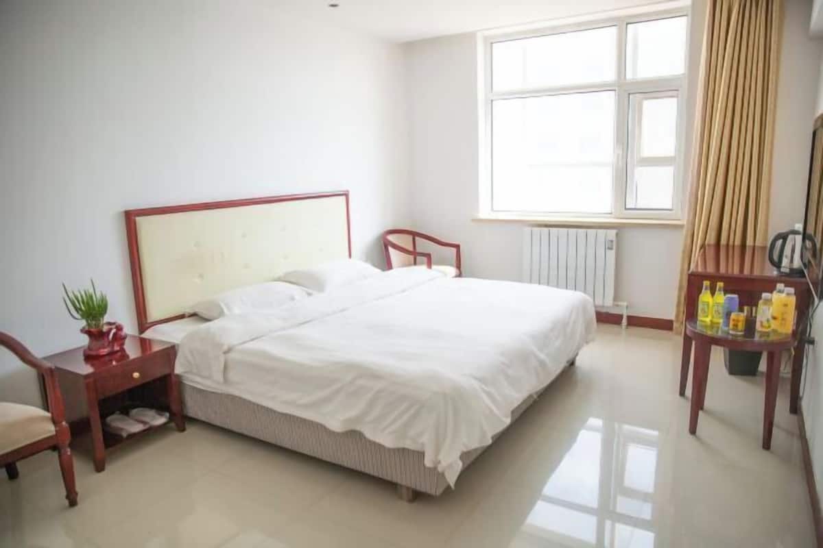 A bedroom with a bed, a nightstand, a chair, a window, and a table with bottles.