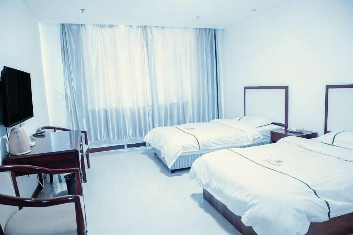 A hotel room with two beds, a desk, a chair, a television, and a window with curtains.