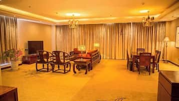 A spacious living room with a large sofa set, a coffee table, and a TV. There are curtains on the windows and a chandelier hanging from the ceiling.