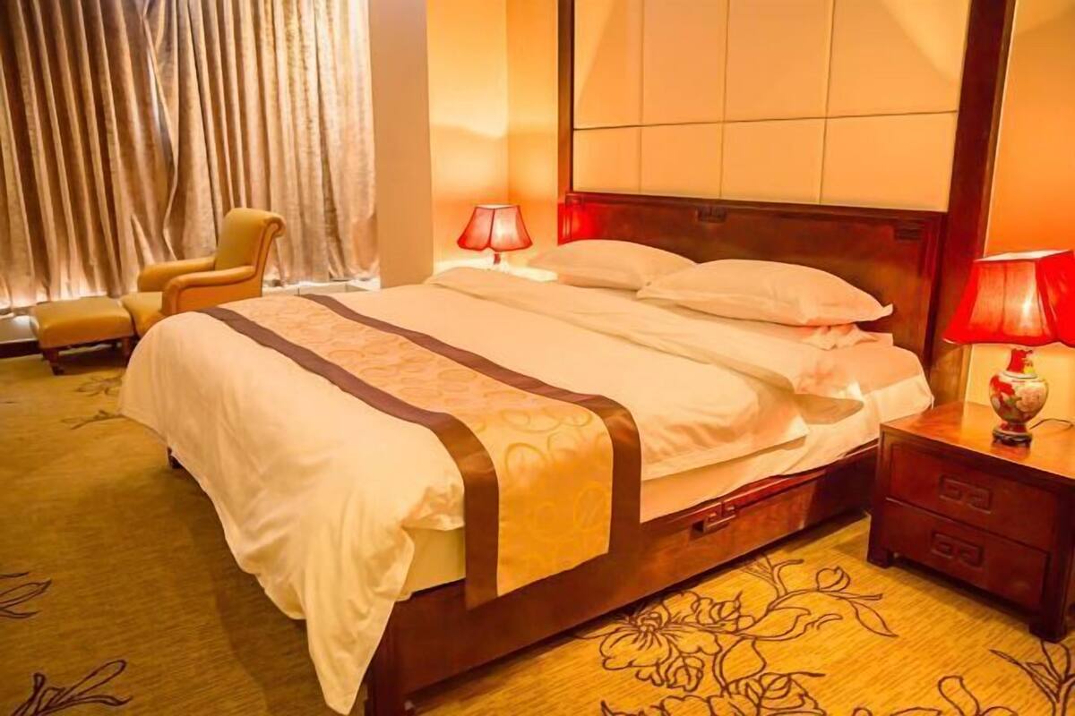 A hotel room with a large bed, a wooden nightstand, a chair, and a window with curtains.