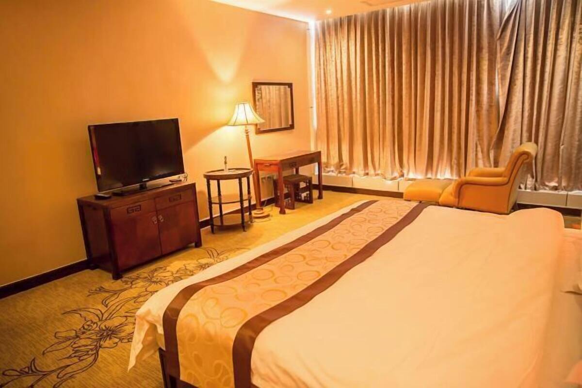 A hotel room with a bed, a television, a desk, a lamp, and a window with curtains.