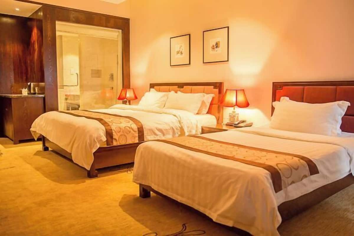 A hotel room with two beds, a wooden headboard, a nightstand with a lamp, and a mirror.