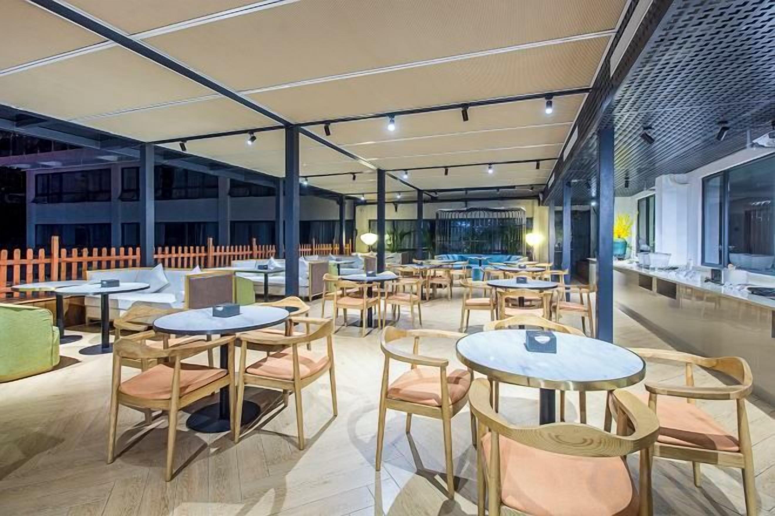 An outdoor seating area with round tables and chairs, covered by a canopy, and a view of the cityscape.