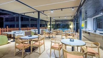 An outdoor seating area with round tables and chairs, covered by a canopy, and a view of the cityscape.