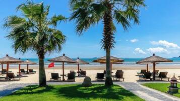 Un resort frente a la playa con palmeras, sillas de playa y sombrillas.