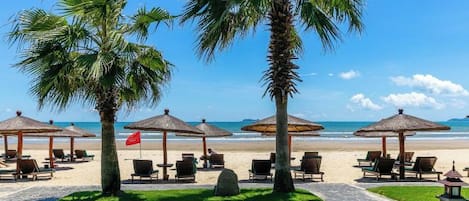 A beachside resort with palm trees, beach chairs, and umbrellas.