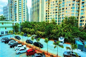 A parking area with multiple cars, surrounded by tall residential buildings and palm trees. - Metropolis Hotel (Sanya Bay Coconut Dream Corridor) (Sanya)