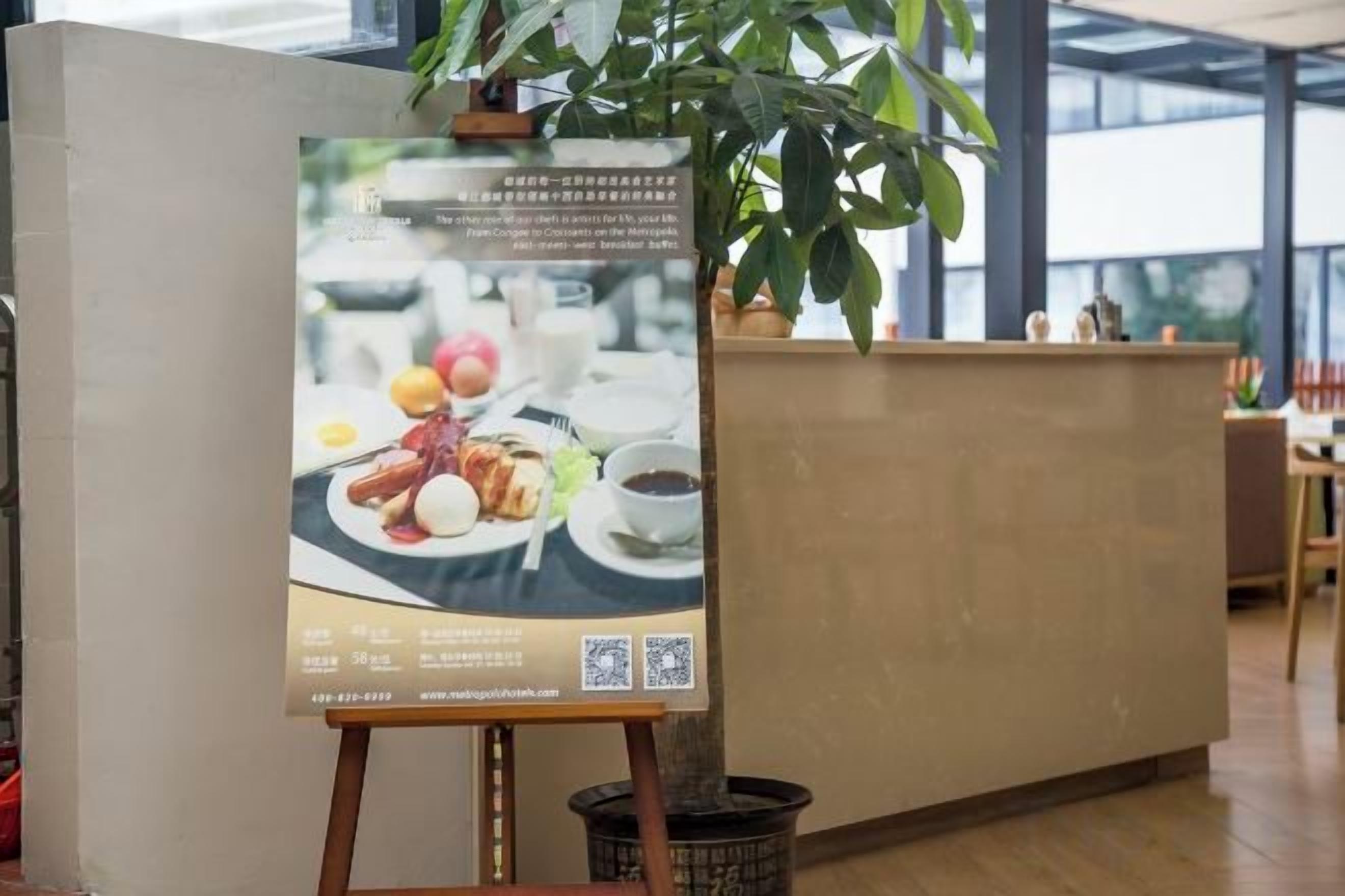 A reception desk with a poster advertising food and beverages, a potted plant, and a view of the outdoors.