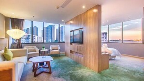 A modern hotel room with a large TV, comfortable seating, a small table, and a view of the city skyline. - Metropolis Hotel (Sanya Bay Coconut Dream Corridor) (Sanya)