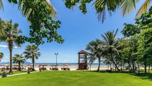 A beachside park with a lifeguard tower, palm trees, and beach umbrellas. - Metropolis Hotel (Sanya Bay Coconut Dream Corridor) (Sanya)