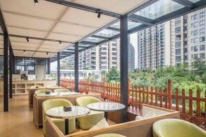 A modern indoor seating area with tables and chairs, large windows, and a view of high-rise buildings. - Metropolis Hotel (Sanya Bay Coconut Dream Corridor) (Sanya)