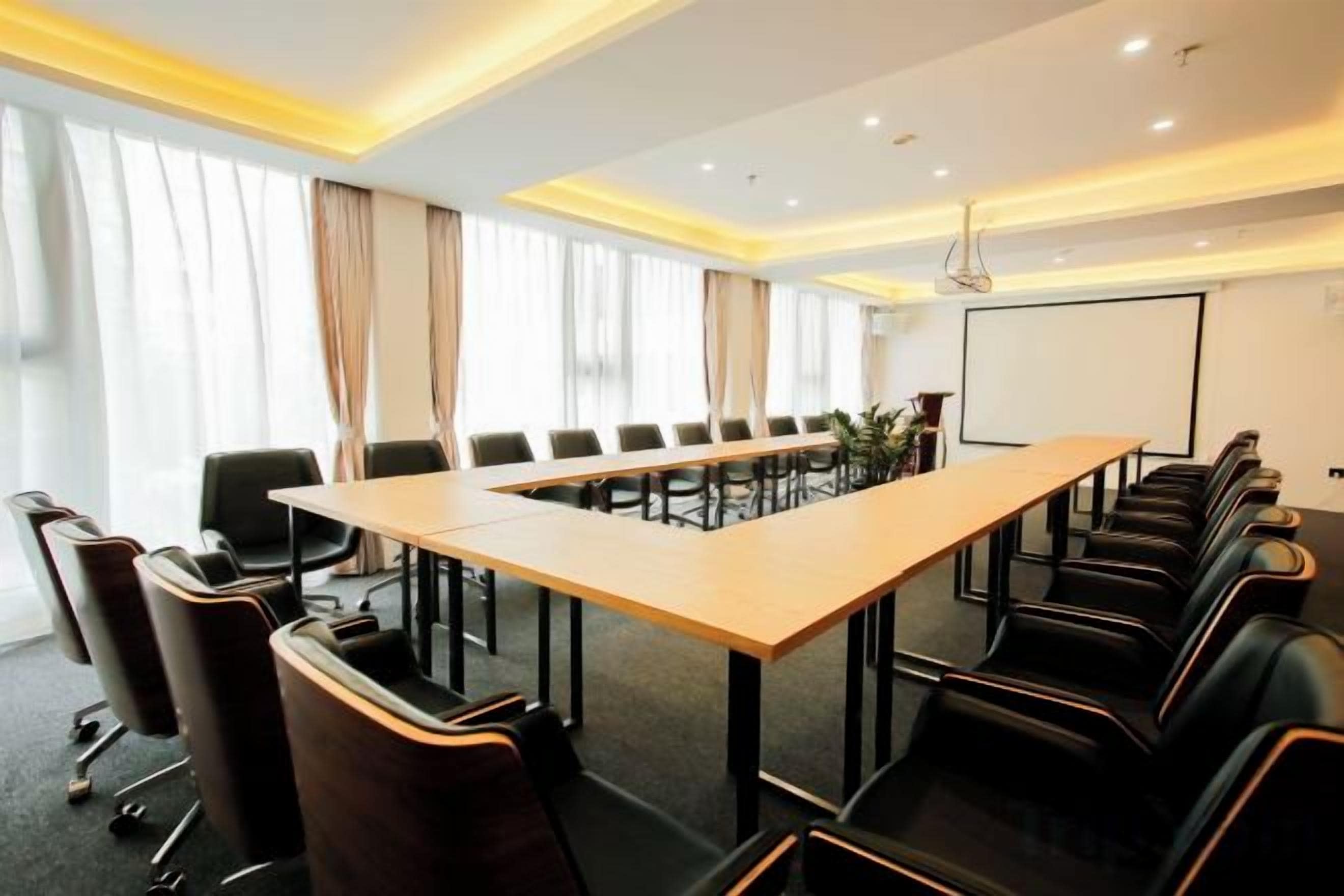 A conference room with a long table, chairs, and a projector screen.