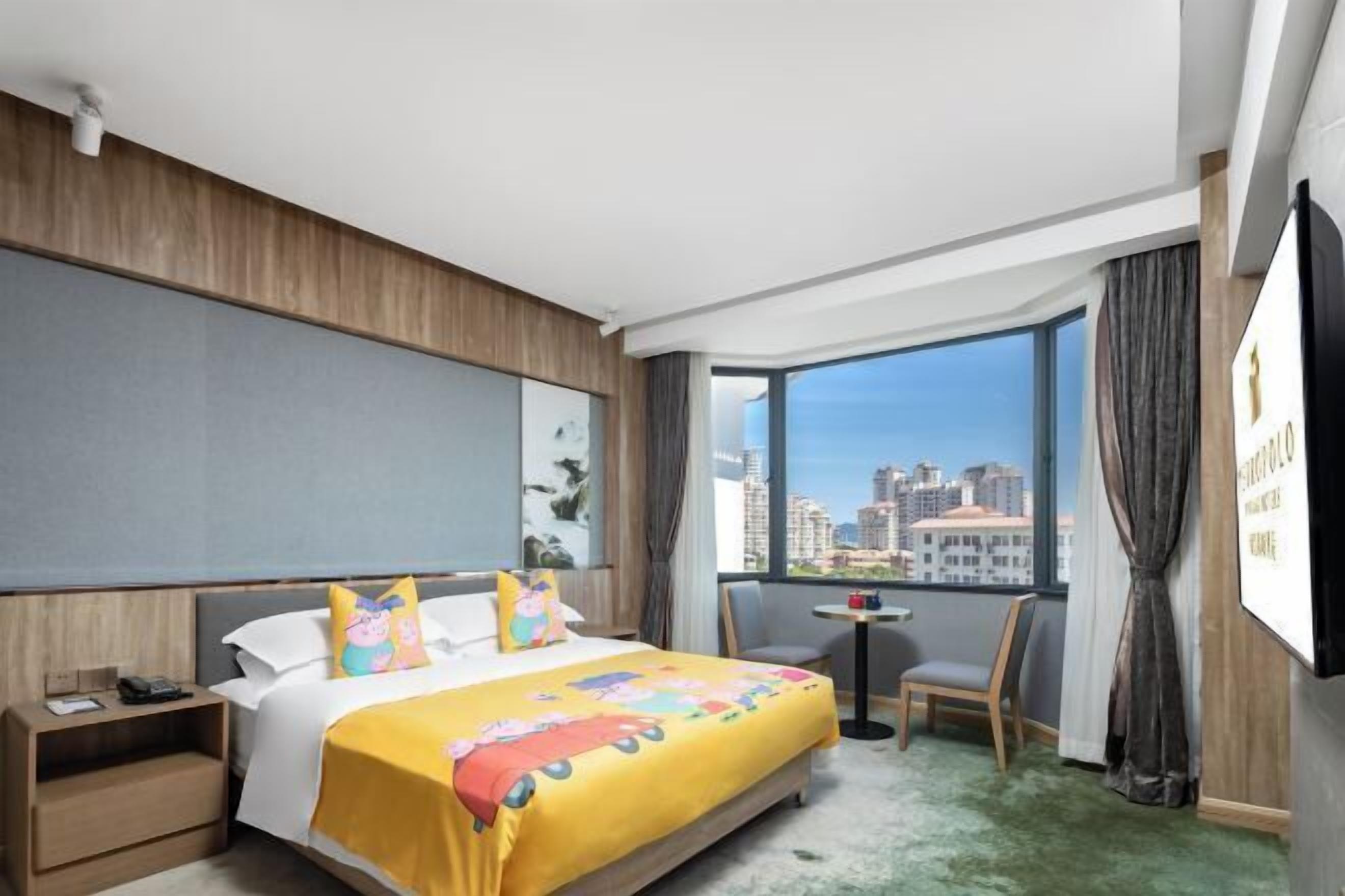 A hotel room with a large bed, a small table, a chair, a TV, and a view of the city.