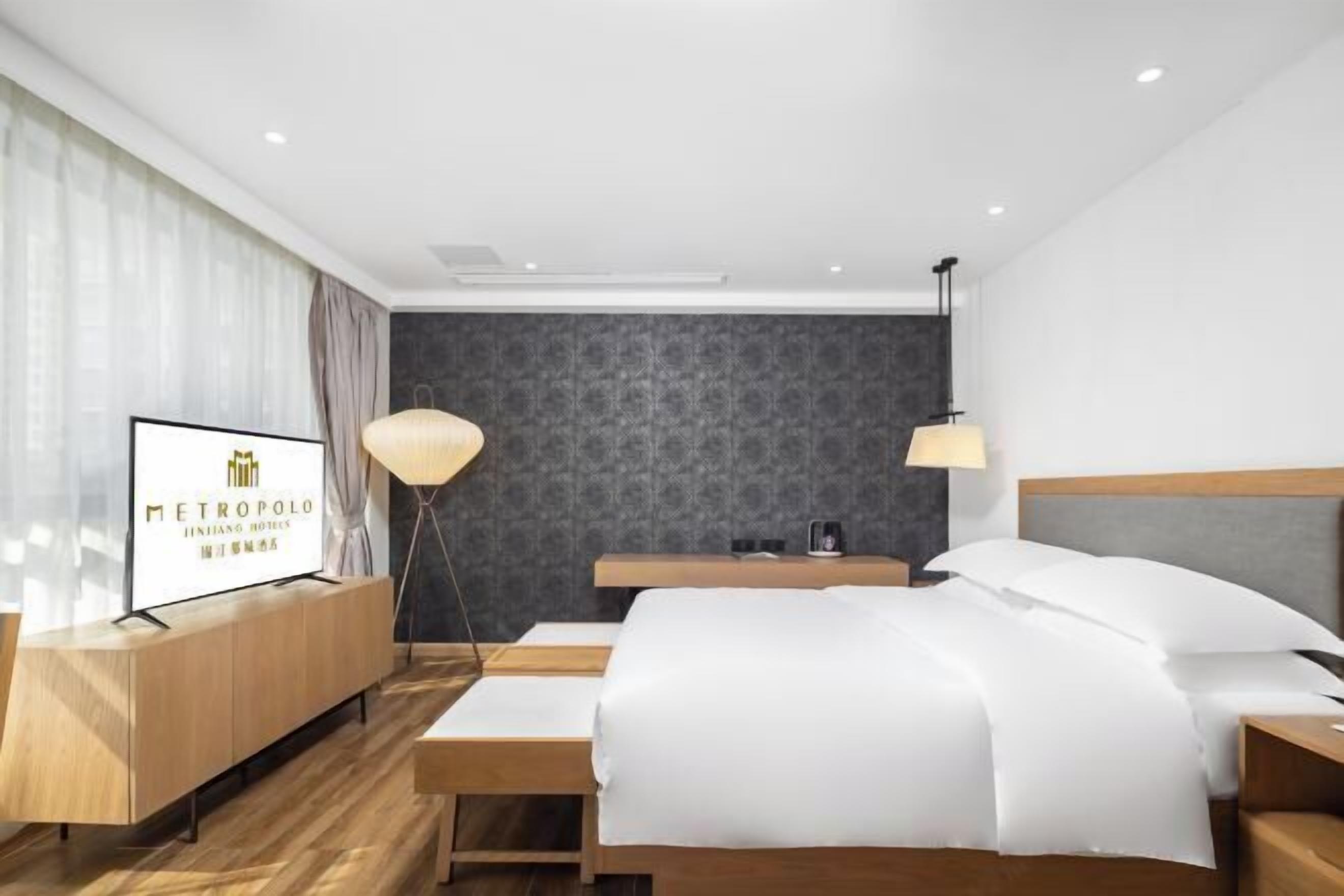 A modern hotel room with a bed, bedside tables, a TV, and a lamp.
