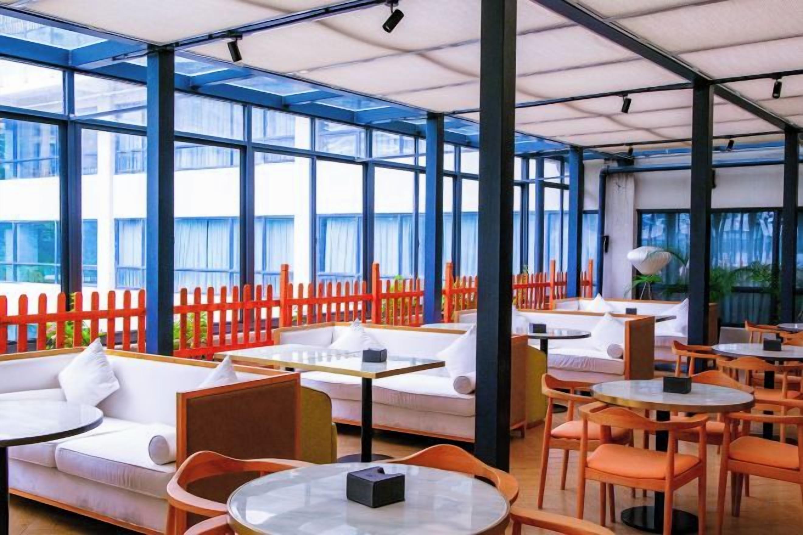 A modern indoor seating area with tables and chairs, large windows, and a red fence.