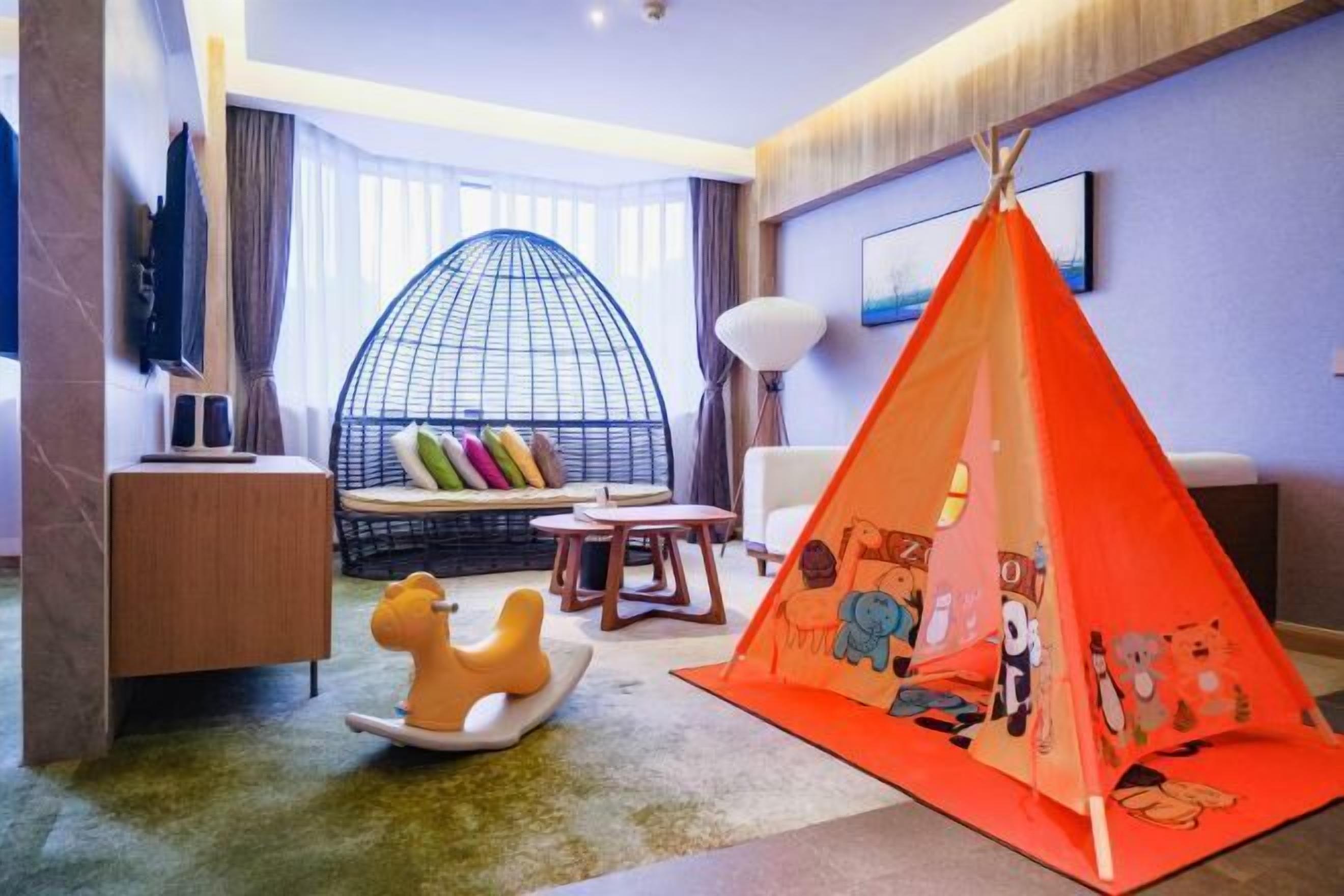 A cozy room with a large window, a comfortable sofa, a small table, and a colorful play tent.