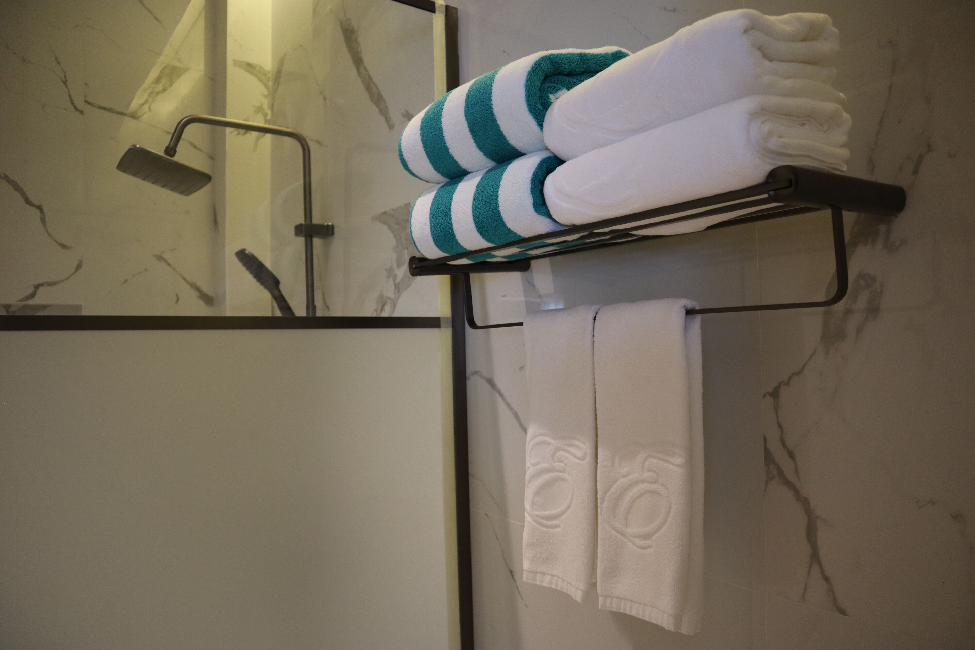 A bathroom with a marble wall, a towel rack with folded towels, and a showerhead.