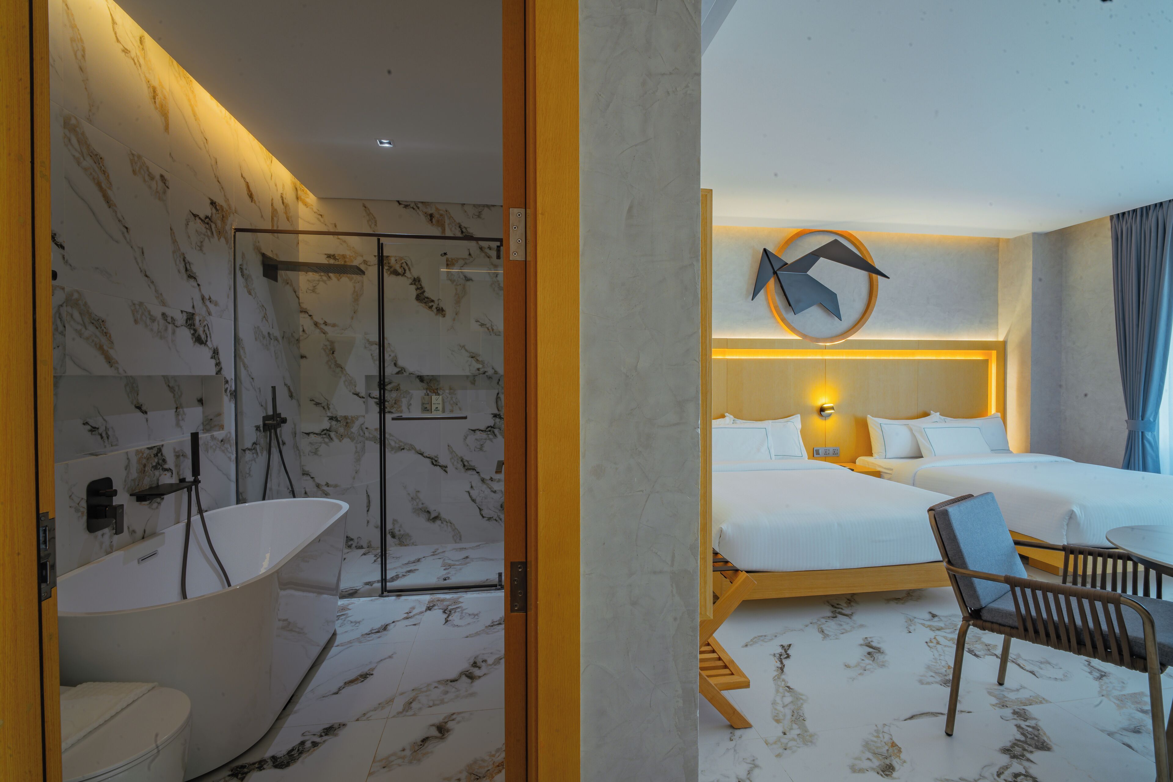 Ett hotellrum med badrum i marmor, två sängar, en trästol och en unik väggdekoration.