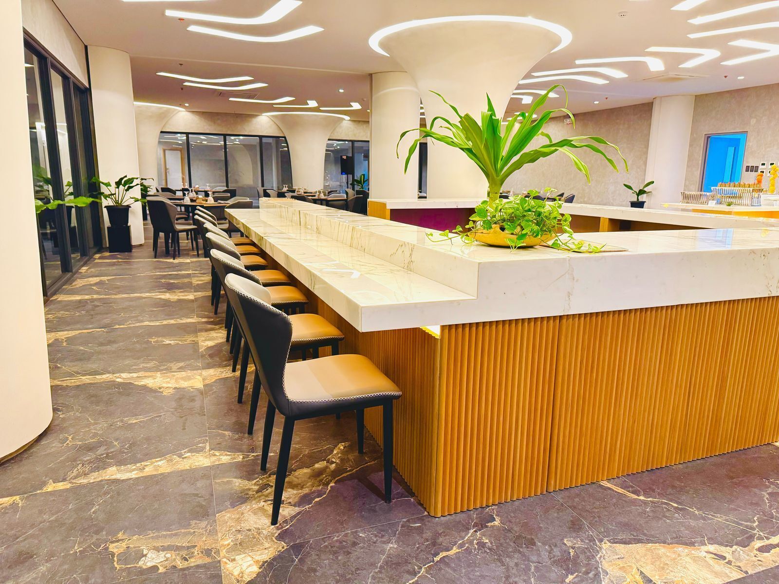 A modern reception area with a marble floor, a central counter with a plant, and multiple seating arrangements.