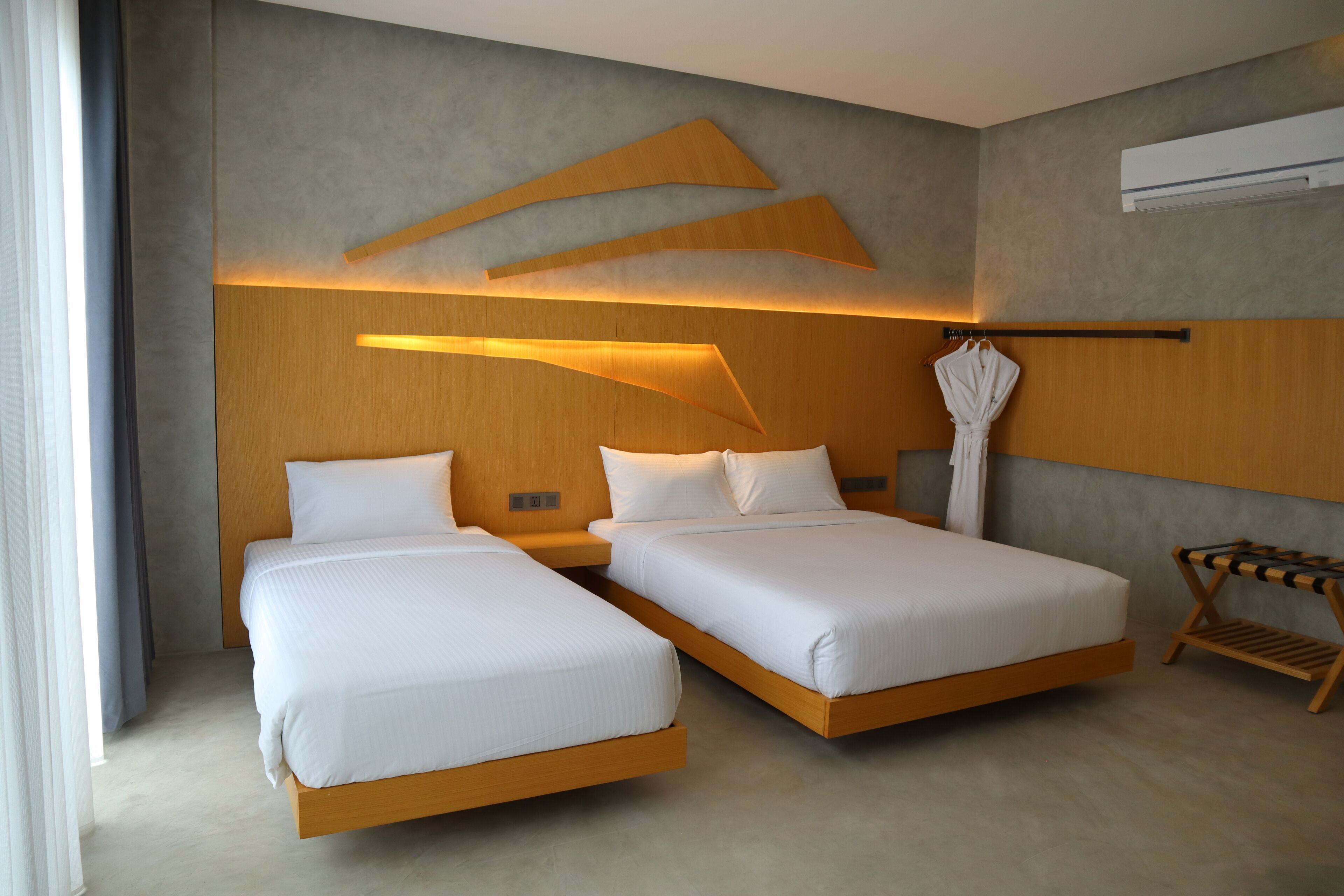 A modern hotel room with two single beds, a wooden headboard, and a wall-mounted air conditioning unit.